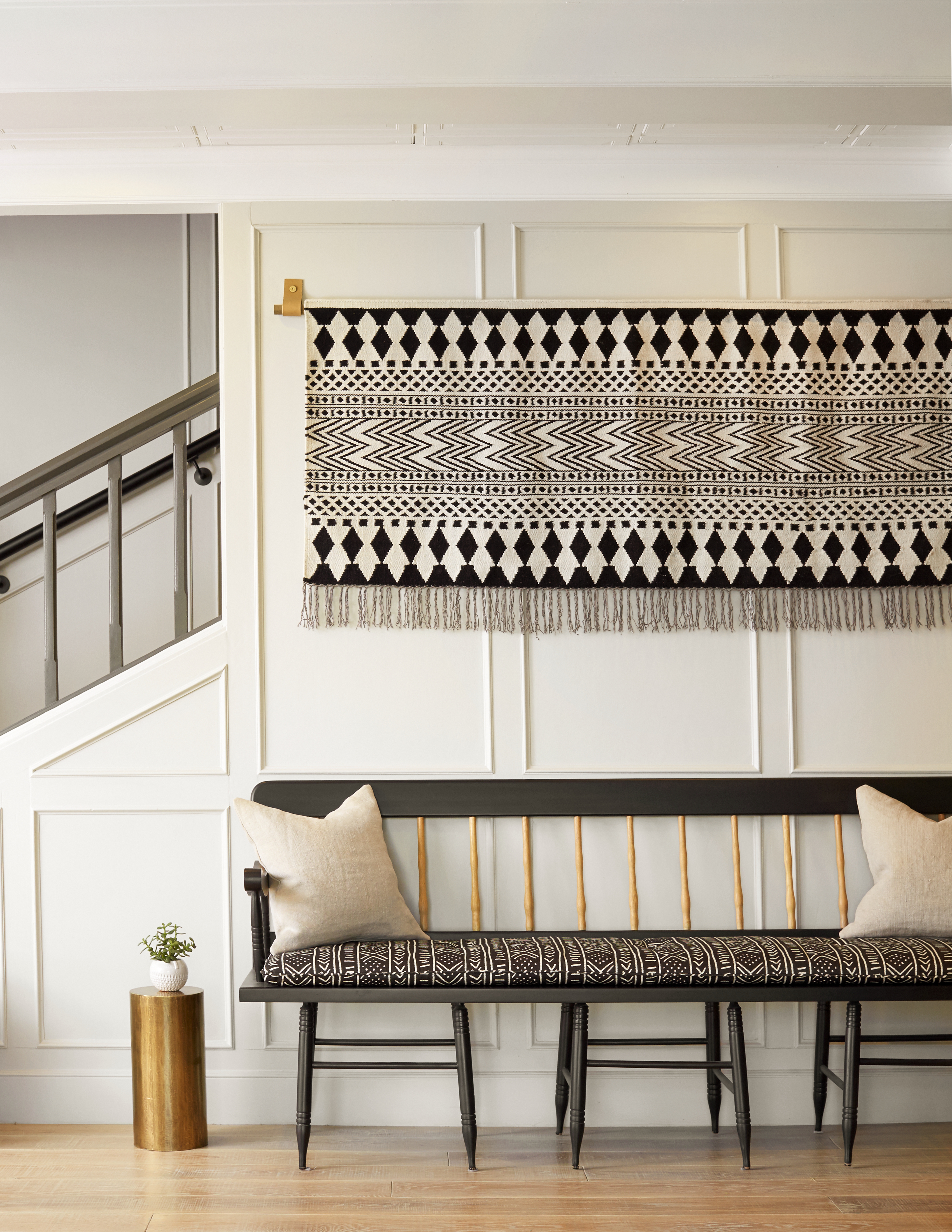 Photo of The Landsby. Scandinavian bench seat design with beige pillows and similiar geometric print wall hanging with stairs to the left.