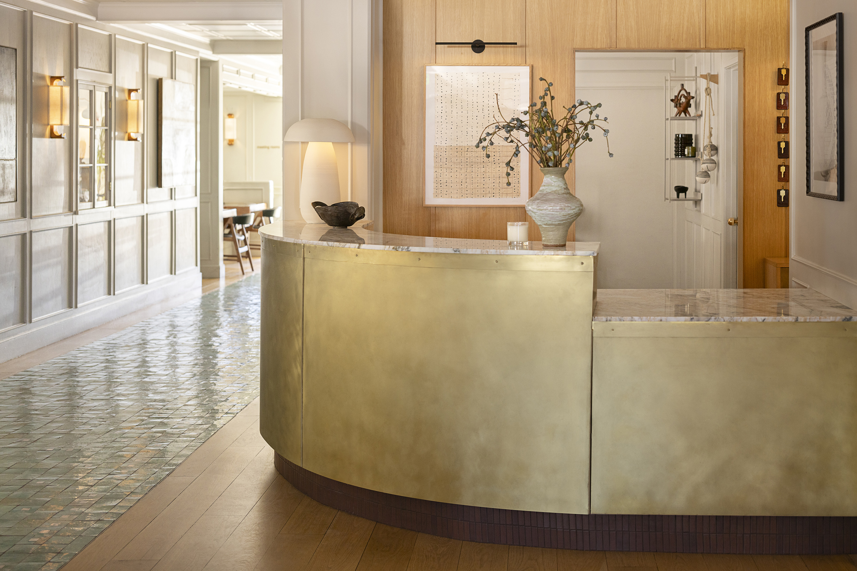 Photo of The Landsby. Guest check-in desk with light walls, modern sconces, pottery vase with dried florals and a candle on the desk.