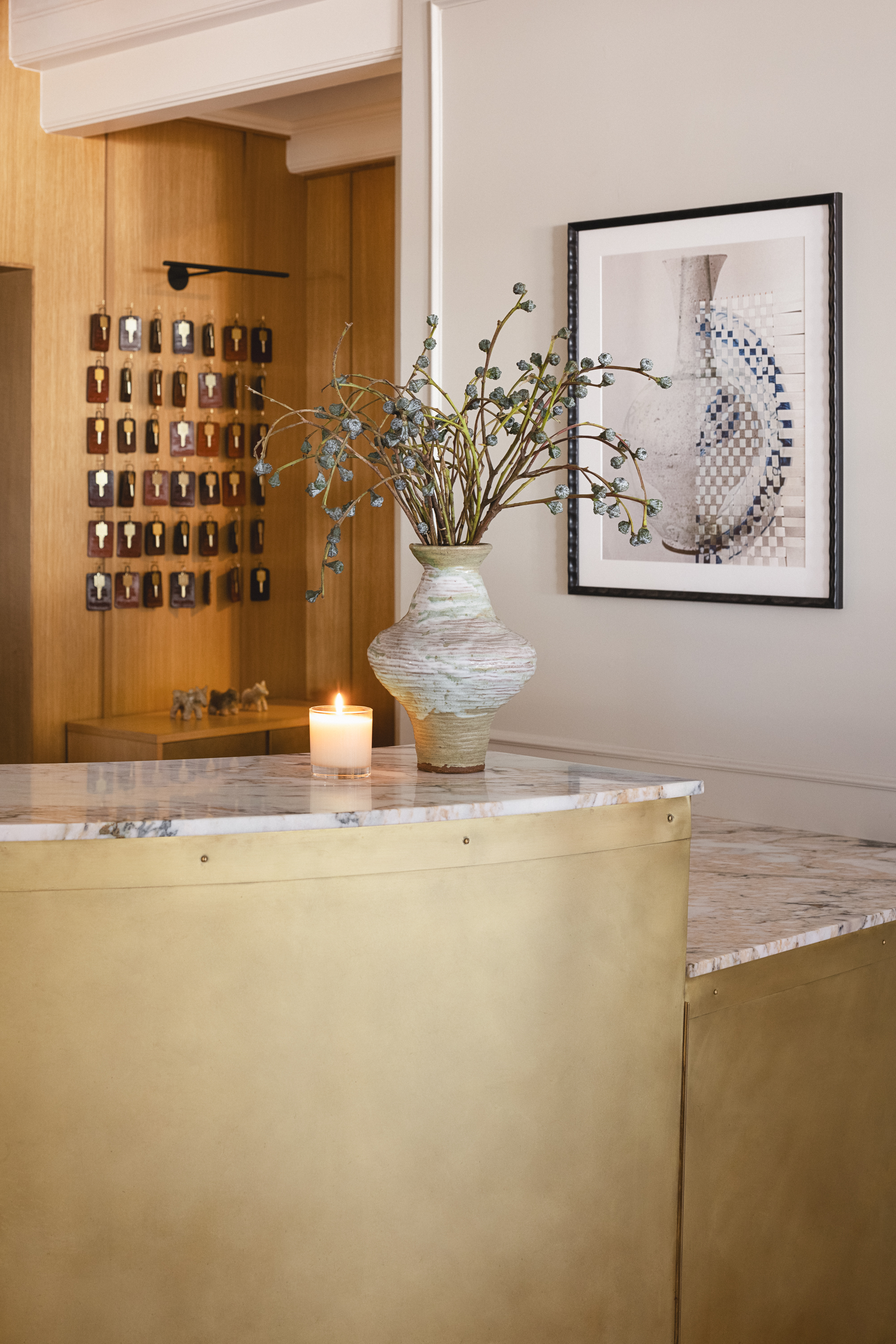 Photo of The Landsby. Guest check-in desk with light walls, modern sconces, pottery vase with dried florals and a candle on the desk.