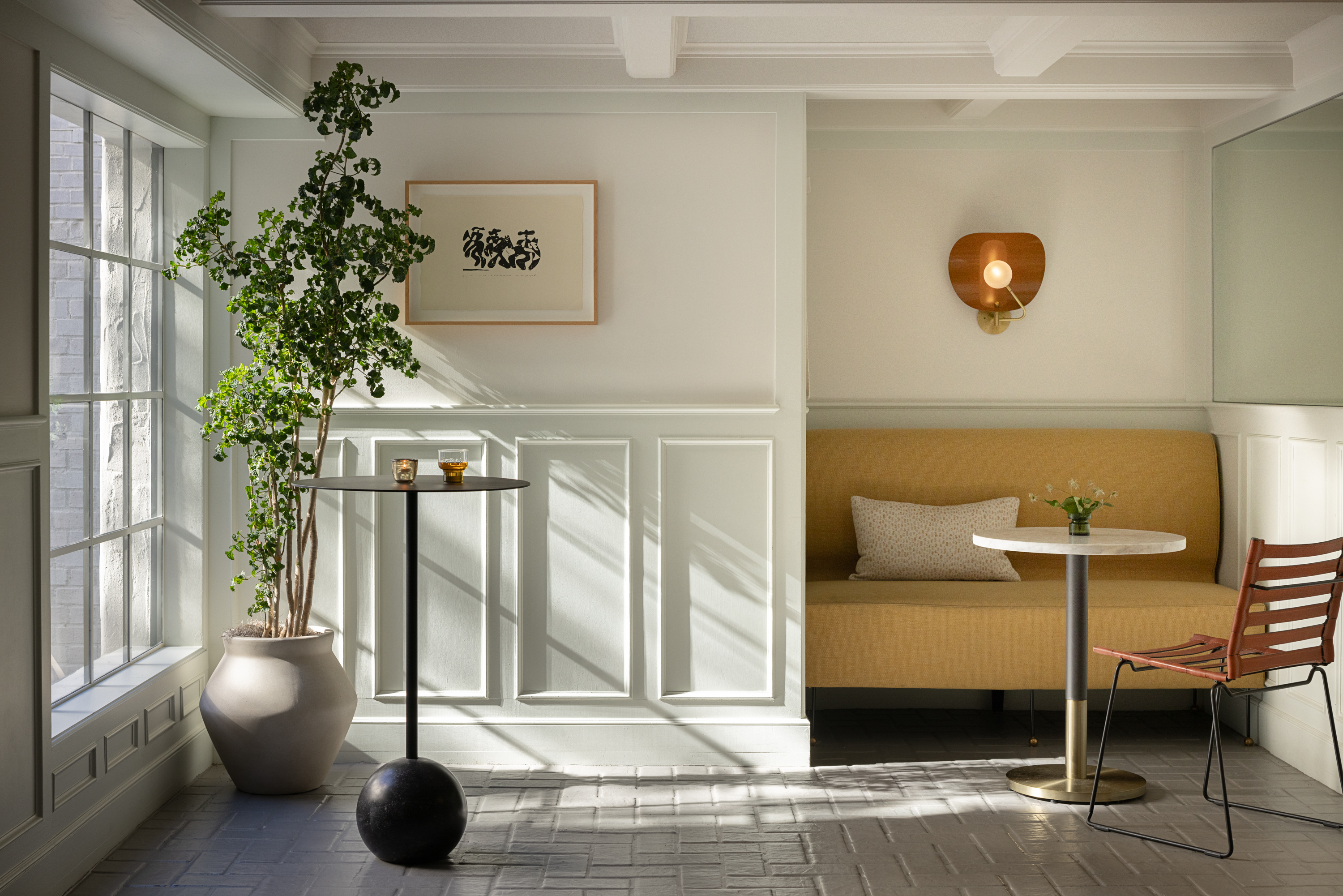 Photo of The Landsby. Seating area in The Mill Bar, reception bar near meeting space. Tall indoor plant in oversized plant pot, modern chair with leather slats, and yellow tuffed seating.