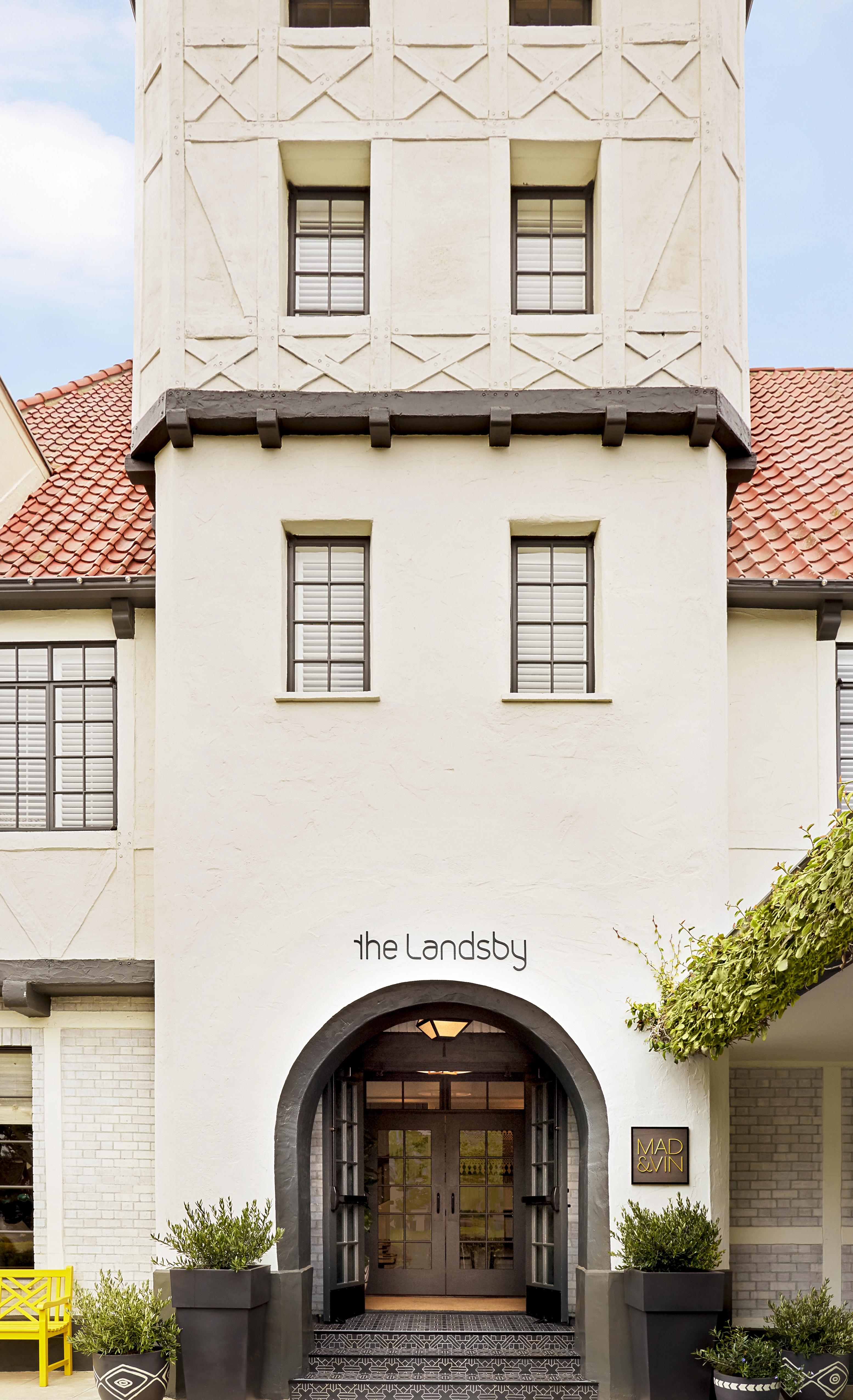 Photo of The Landsby. The entrance of The Landsby hotel features an arched doorway, potted plants, and a sign for Mad & Vin restaurant, set in a light-colored, half-timbered building with red roof tiles and multiple windows.