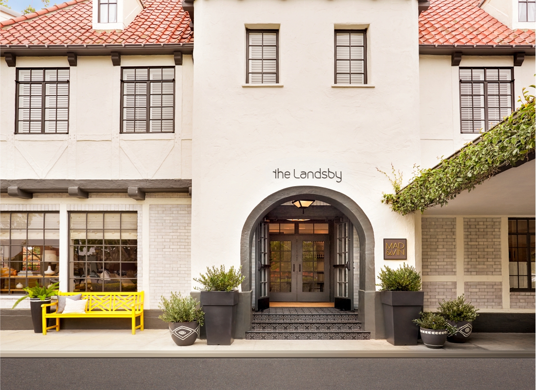 Photo of The Landsby. The entrance of The Landsby hotel features an arched doorway, large potted plants, and a bright yellow bench beside a window; the building has white walls and a red-tiled roof. Contact The Landsby to learn more about this inviting space.