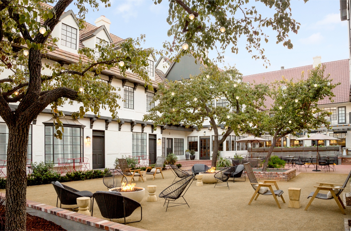 Photo of The Landsby. A charming outdoor courtyard showcases Hotel Amenities at The Landsby, with modern lounge chairs around fire pits, string lights in trees, and a cozy ambiance. The space is framed by buildings with white walls and red-tiled roofs.