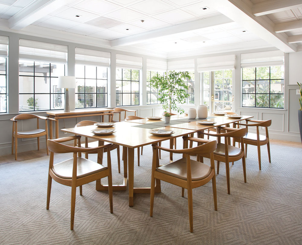 A bright, modern dining room with large windows doubles as one of the inviting event spaces in Solvang. A wooden table set for eight, matching chairs, and neutral decor create a minimalist design flooded with natural light.
