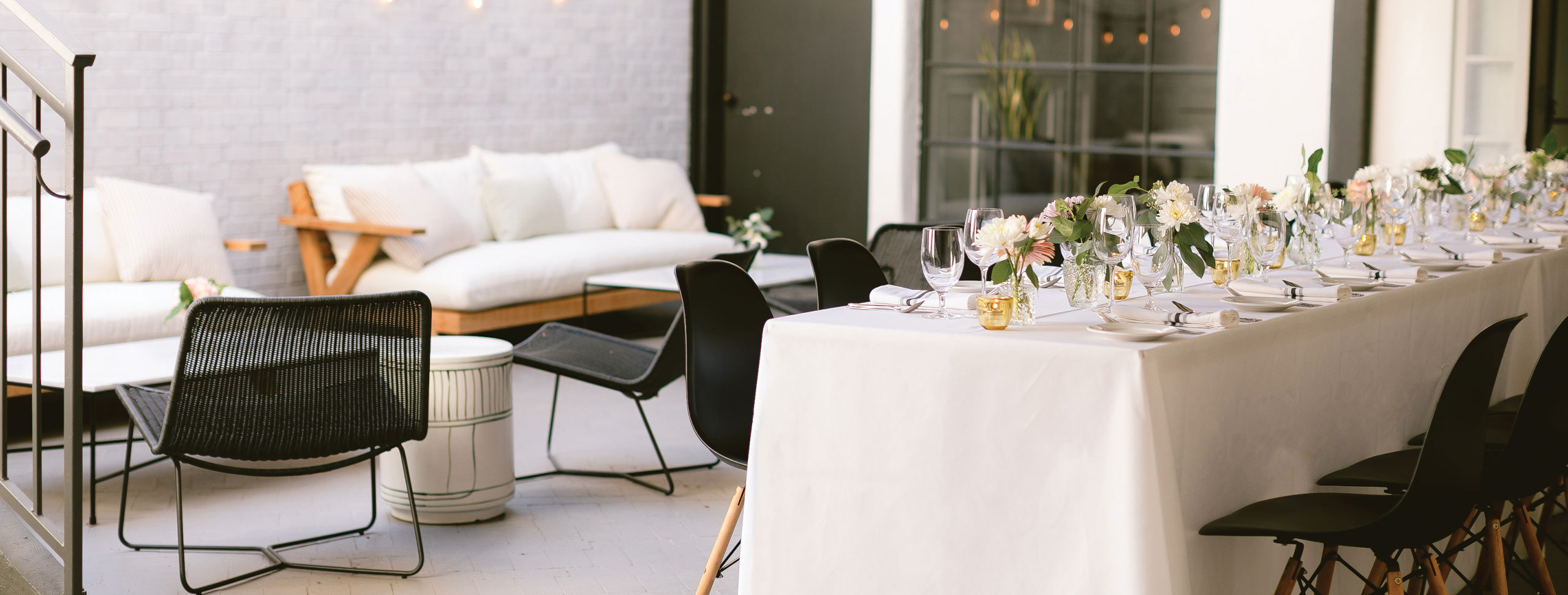 A long, elegant table with white linens and floral centerpieces is set for a gathering. Black chairs line the table, while cozy sofas sit in the background, highlighting the modern charm of event spaces in Solvang.