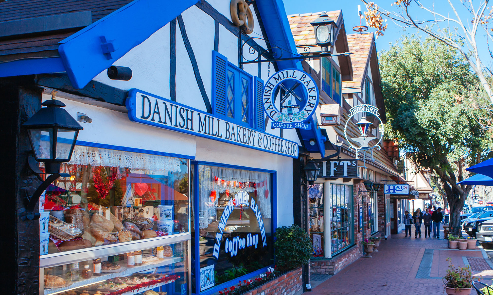 A charming street in Solvang, California, features Danish-style architecture. Among the top things to do in Solvang are visiting shopfronts like Danish Mill Bakery & Coffee Shop, where baked goods tempt pedestrians strolling the sidewalk.